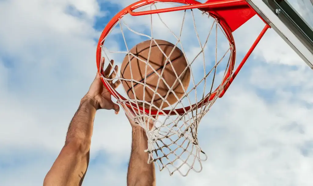 Gros plan sur un ballon de basket passant dans le panier par le bas, sur fond de ciel lumineux, mettant en valeur les détails du filet et de l'anneau
